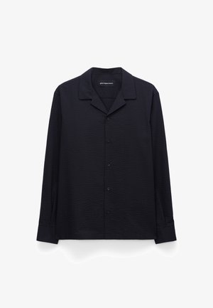 Chemise noire à manches longues avec boutons, en tissu texturé et col pointu, posée à plat sur un fond blanc.