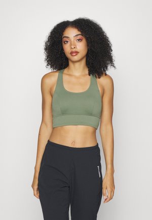 Top court côtelé vert olive avec de larges bretelles et un col rond. Associé à un pantalon noir avec un détail de logo sur le côté.