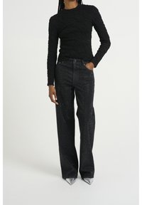 Top negro de mangas largas con un patrón texturizado, combinado con jeans negros de talle alto y pernera ancha con detalles de rhinestones y zapatos puntiagudos plateados.