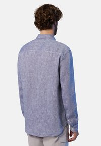 Camicia di lino blu con taglio dritto, maniche lunghe, polsini con bottoni e una texture morbida. Presenta un colletto classico e un delicato motivo tessuto.