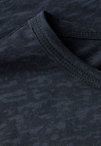 T-shirt gris foncé avec une texture subtile, présentant un col rond et un détail de couture contrastant. Vue rapprochée sur le tissu.