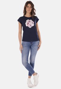 T-shirt navy a maniche corte con grafica floreale. Abbinato a jeans blu chiaro e scarpe da ginnastica bianche. Materiale in cotone, vestibilità rilassata.