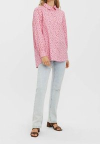 Pink long-sleeve shirt with a collar, featuring a small floral pattern. Paired with light blue jeans and brown block-heeled sandals.