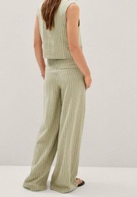 Jasnozielony, bezrękawnikowy crop top i spodnie w szerokich nogawkach z subtelnymi pionowymi paskami. Materiał wydaje się teksturowany; spodnie opadają do podłogi.