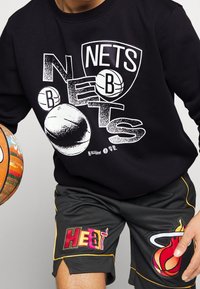 Felpa nera con stampa grafica che presenta il termine "Nets" e motivi di basket. Abbinata a pantaloni corti neri con il logo "HEAT" e accenti rossi.