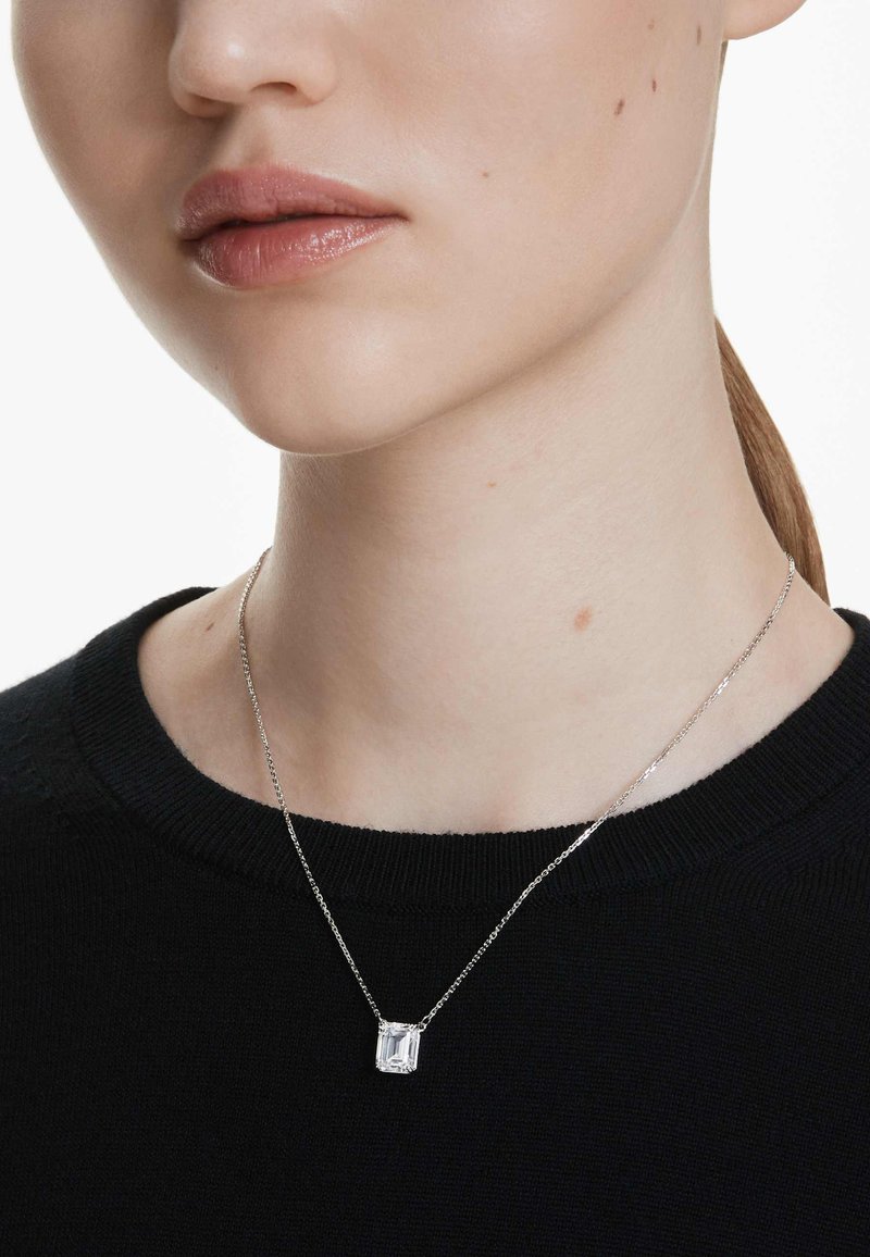 Collana in argento con pendente rettangolare trasparente, indossata sopra un maglione nero, che mette in risalto il suo design semplice ed elegante.
