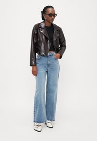 Καφέ, γυαλιστερό, κοντό δερμάτινο μπουφάν; μαύρη ριμπ παντελόνα; ανοιχτό μπλε σαρώμα με φαρδιά πόδια; λευκά και ασημένια παπούτσια με λουριά; σκούρα γυαλιά ηλίου.