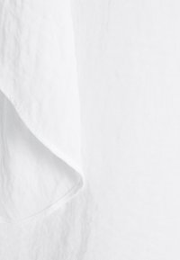 Gros plan sur un coin de tissu en lin blanc avec une texture visible et des coutures soignées le long du bord.