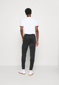 Pantaloni della tuta neri con una vestibilità affusolata, vita elastica e polsini a coste, abbinati a una maglietta bianca a maniche corte e sneakers bianche.