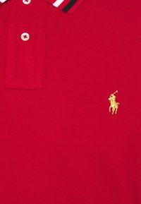 Czerwona koszulka polo wykonana z teksturowanej tkaniny, charakteryzująca się jednolitym wzorem, z plisą na dwa guziki oraz złotym haftowanym logo przedstawiającym jeźdźca.