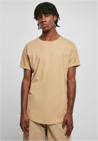 Tricou scurt cu mâneci scurte, de culoare bej, cu guler rotund, croială lejeră și textură moale din bumbac. Cusături minime și fără modele sau grafice vizibile.