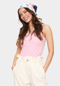 Svjetloružičasti rebrasti top na bretele uparan s kremasto visokim hlačama visokog struka s elastičnim pojasom i džepovima. Šal s printom u šarenim uzorcima.