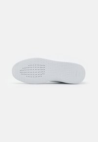 Sole di sneaker bianca con una finitura liscia e texture, e perforazioni per la traspirazione. Presenta il marchio sul tallone.