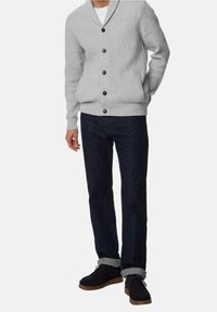 Grau gestrickte Strickjacke mit Schalkragen, Knopfverschluss und Seitentaschen, kombiniert mit dunkelblauen Jeans und schwarzbraunen Schuhen.