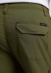 Des shorts cargo en coton mélangé vert avec des poches plaquées, des coutures visibles et une étiquette près de la taille. Texture douce avec une finition mate.