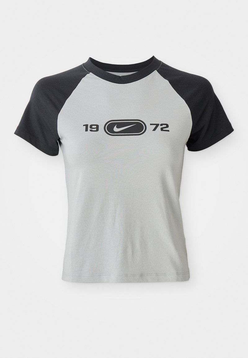 Camiseta de manga corta en gris y negro, con un escote redondo, que presenta un logo central y el texto "1972" en negro en la parte delantera.