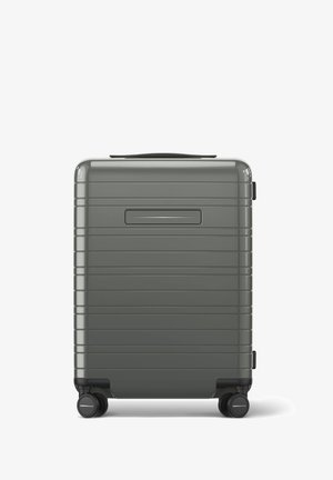 Valise rigide de couleur grise atténuée, présentant une surface texturée avec des lignes verticales, une poignée supérieure et quatre roues noires pour la mobilité.