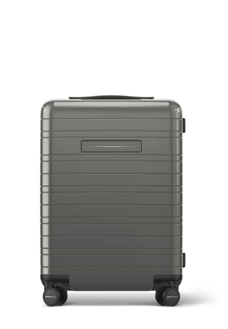 Valise rigide de couleur grise atténuée, présentant une surface texturée avec des lignes verticales, une poignée supérieure et quatre roues noires pour la mobilité.