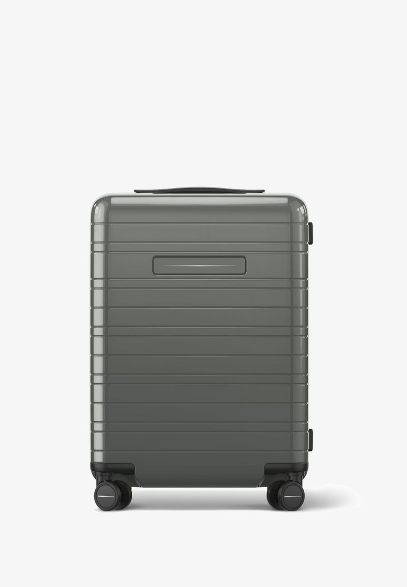 Valise rigide de couleur grise atténuée, présentant une surface texturée avec des lignes verticales, une poignée supérieure et quatre roues noires pour la mobilité.