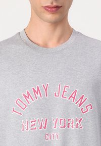 Szara bawełniana koszulka z okrągłym dekoltem i nadrukiem, który brzmi "TOMMY JEANS NEW YORK CITY" w różowym kolorze.