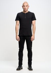 Černé žebrované tričko s krátkým rukávem a knoflíkovou légou, v kombinaci s černými slim-fit džíny a černými šněrovacími botami. Jednoduchý design, žádné vzory.