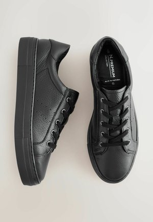 Juodi odiniai sportbačiai su tekstūruotu paviršiumi, apvaliu priekiu, šešiais akių skyreliais ir gumine padu. Minimalistinis dizainas ir švarios linijos.