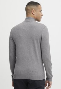 Grau Pullover mit hohem Kragen, langen Ärmeln und taillierter Passform. Hergestellt aus weichem Material mit gerippten Bündchen und Saum.