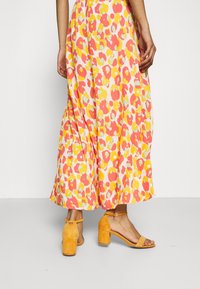 Maxiklänning med ett djärvt leopardmönster i rosa, gult och grönt; matchad med sandaler med blockklack i orange mocka.