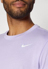 Lilac crew neck T-shirt made of soft cotton fabric featuring a small white Nike swoosh logo on the upper left chest area.
