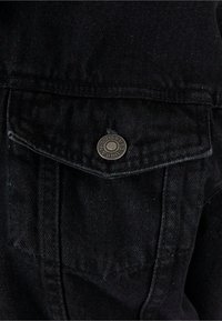 Zwart denimstof heeft een voorzak met een puntige klep en een metalen knop met "Urban Classics" erop gegraveerd.