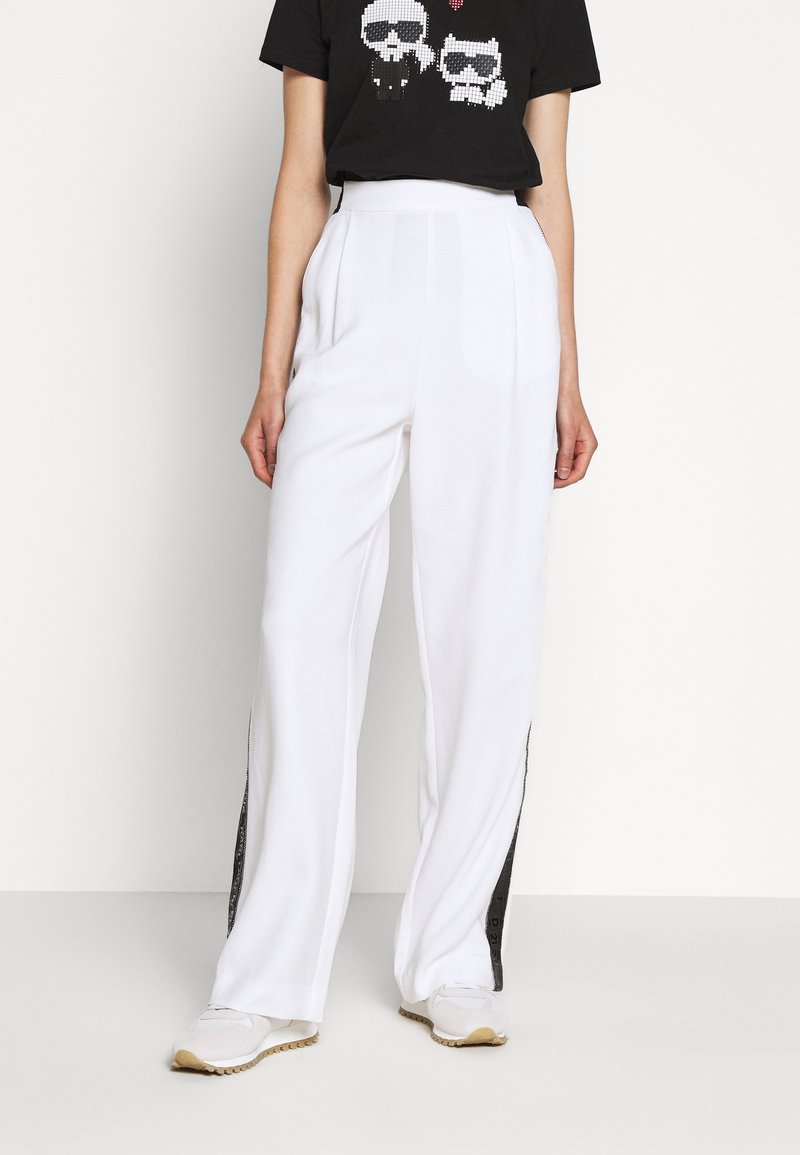 Pantalon blanc à jambes larges en tissu doux avec une bande latérale noire. Associé à un t-shirt noir à motifs graphiques avec des designs de crânes.