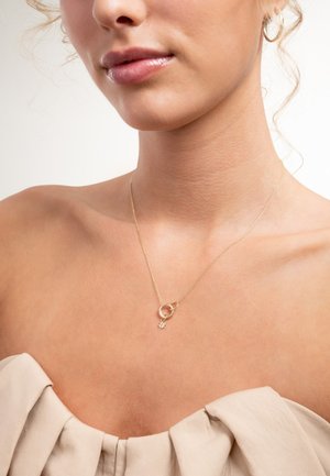 Gouden ketting met een ontwerp van onderling verbonden cirkels en een kleine bloembedel. De ketting is fijn en complimenteert een blote schouder.