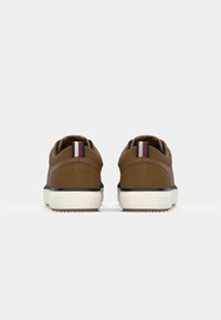 Brune semskede sneakers med en hvit såle, svarte detaljer og et stripete element på baksiden. Rund form med polstret hæl.