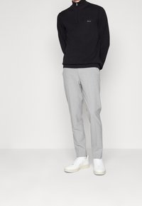 Zwarte gebreide half-zip trui, grijze op maat gemaakte broek en witte sneakers. De trui heeft een subtiele logo en de broek heeft een gladde textuur.