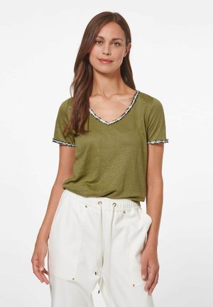 Olijfgroene V-hals t-shirt met korte mouwen, versierd met zwart-witte franjes op de halslijn en mouwen, gemaakt van zachte, lichte stof.