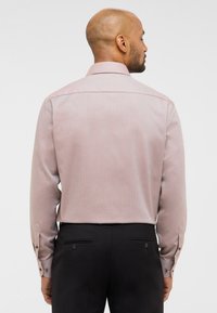 Lange mouwen, lichtroze shirt met een gestructureerd patroon en geknoopte manchetten. Getoond vanuit de achterkant, gecombineerd met donkere broek.