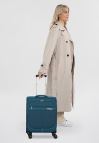 Teal soft-shell koffer met ritssluiting, voorvak en vier wielen. Voorzien van een uittrekbare handgreep en een accentlijn in het groen.