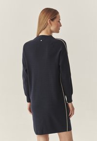 Navy-Strickkleid mit langen Ärmeln, lockerer Passform und kontrastierenden hellbeigen Seitenstreifen. Verfügt über ein kleines Knopfdetail am Rücken.