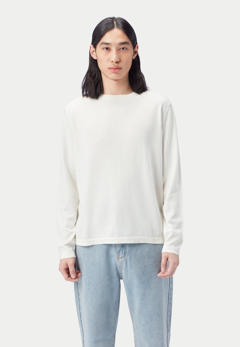 Weißes Langarm-T-Shirt aus weicher Baumwolle mit Rundhalsausschnitt, kombiniert mit hellblauen Jeans, vor neutralem Hintergrund gezeigt.