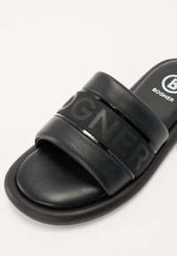 Svarte sandaler laget av lær med to brede stropper; en teksturert stoffrem med hevet logo og en blank aksent.
