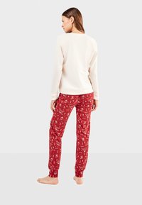 Haut crème à manches longues associé à un pantalon de pyjama rouge présentant un motif amusant d'animaux blancs. Tissu doux avec des poignets et une taille côtelés.