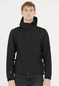 Mustat vedenpitävät takki, jossa on huppu, vetoketjulliset taskut, säädettävät hihansuut ja virtaviivainen muotoilu. Päällä musta paita.