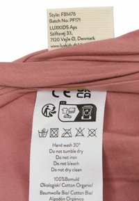 Étiquette de vêtement sur tissu rose indiquant des symboles d'entretien et des instructions pour le lavage à la main, pas de séchage en machine, pas de repassage, pas de blanchiment et pas de nettoyage à sec.