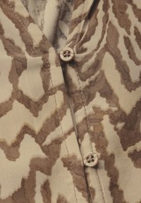 Gros plan sur un tissu à motif zigzag beige et marron avec deux petits boutons beiges cousus le long d'une couture.