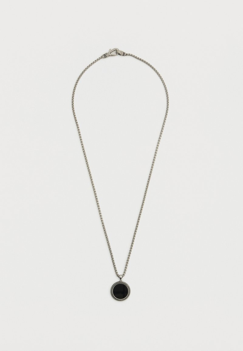 Collier en ton argent avec un pendentif rond noir, bordé de perles. La chaîne est fine, texturée et se ferme par un fermoir.