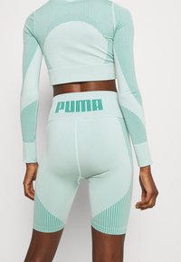 Mintgrüne Sportkleidung mit einem taillierten, kurz geschnittenen Oberteil mit strukturiertem Muster und hochgeschnittenen Shorts, die einen Logo-Bund aufweisen.