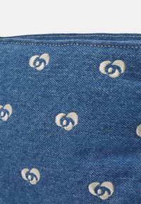 Modrá džínovina s opakujícím se vyšívaným vzorem spletených srdcí v krémové barvě. Textura je klasická a mírně hrubá.