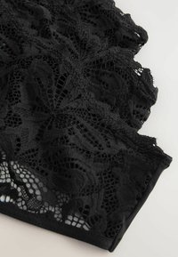 Sort blonderstof med indviklede blomsterbortmønstre og en tekstureret finish. Kanterne er bølgede og giver et halvtransparent udseende.