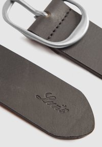 Gros plan de l'extrémité d'une ceinture en cuir noir avec le logo embossé "Scarti" et une boucle en métal argenté sur fond blanc.
