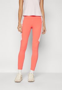 Coral leggings with mesh side panels, textured fabric, slim fit, paired with light beige athletic shoes and white crew socks.